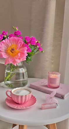 pink flowers in a glass vase on a table with books and candlelight holder next to it