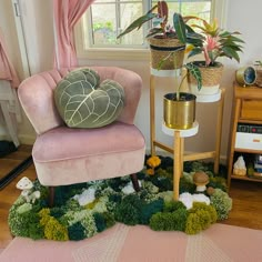 a pink chair sitting in front of a window next to a potted plant on top of a wooden table