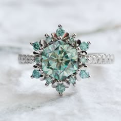 "Reflecting the striking individuality, purity, and symmetry of a snowflake, our Nieva ring features an ice-blue moissanite center stone in a unique, hexagonal cut. A masterfully crafted setting, light-blue moissanite accents, and a sparkle-encrusted band glows in glacial glamour. Matching band sold separately. Sizes 6 & 7 in 14K white gold ready to ship. Quantity limited. Additional sizes and metal options available made-to-order here: https://etsy.me/3CpNkZM ◊ DETAILS ◊ Center Stone: - Type: Moissanite - Size: 7.5 mm (2ct diamond equivalent) - Color: Ice Blue - Cut: Hexagon Setting: - Accented with round brilliant cut ice blue moissanite - Moissanite encrusted band - 14K White Gold - 1.8 mm wide band - Sits ~7 mm (.28\") off the finger ◊ CUSTOMIZATION ◊ Any designs in our current collect Snowflake Ring, Blue Moissanite, Future Engagement Rings, Blue Snowflakes, Cute Rings, Matching Band, Pretty Rings, Fantasy Jewelry, Dream Jewelry