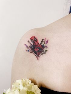 a woman's shoulder with a deadpool tattoo on it and flowers in the background