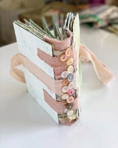 an open book with buttons on it sitting on top of a white table next to other books