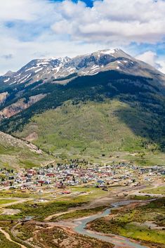 an aerial view of a small town in the middle of a mountain range with snow capped mountains behind it