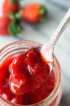 a spoon full of strawberry jam with strawberries in the background