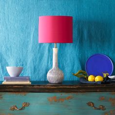 a lamp on a table next to plates and lemons with a blue wall in the background