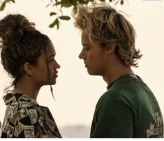 a man and woman standing next to each other under a tree in front of the ocean