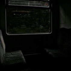 an empty seat sitting next to a window in a dark train car with the light shining on it