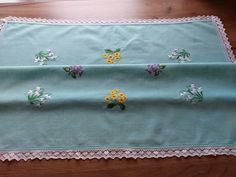 a blue table cloth with flowers and lace on the edge is sitting on a wooden floor