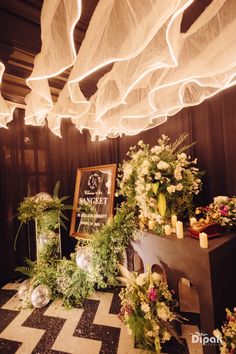 an arrangement of flowers and greenery in front of a sign