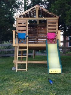 a wooden play structure with a slide in the grass