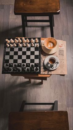 a chess board, coffee cup and other items on a wooden table with two chairs