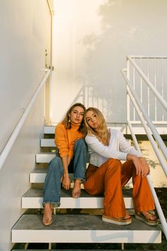 two young women sitting on the steps of a white building, one with her arm around the other's shoulder