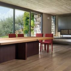 a large table with red chairs in front of a stone wall and floor to ceiling windows