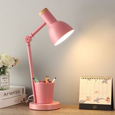 a pink desk lamp sitting on top of a table next to a calendar and pen holder