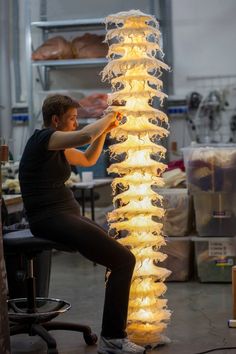 a man sitting on a chair next to a tall light fixture in a room filled with boxes