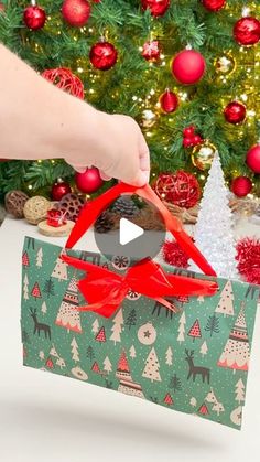 a person opening a christmas present in front of a tree with red bows and ornaments