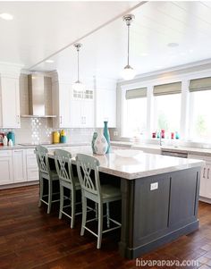 a large kitchen with white cabinets and wooden floors is pictured in this image, there are four green chairs at the center island