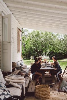 two women sitting at a table on a porch with wicker chairs and pillows around it