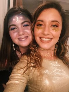 two girls with face paint and gold make - up posing for the camera, both smiling