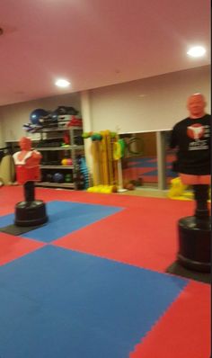 an indoor gym with blue, red and yellow squares on the floor as well as two men in black t - shirts