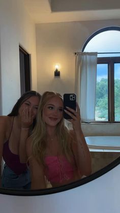 two beautiful young women taking a selfie in front of a mirror