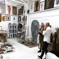 two people are looking at art on display in a room with many framed pictures and paintings