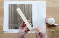 a person is painting on a piece of wood with white paint and some brown paper