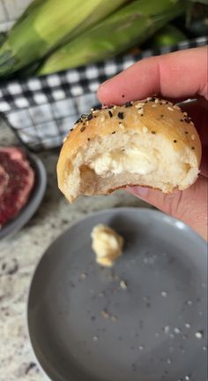 a hand holding a half eaten bagel over a plate with other food items in the background