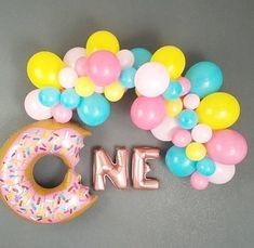 a doughnut with balloons and the word one spelled out in gold letters on a gray surface