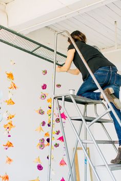 a woman on a ladder painting flowers on the wall in an arts and crafts studio