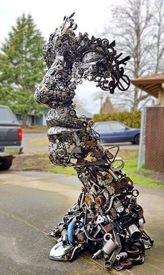 a large metal sculpture sitting on top of a parking lot next to a car parked in front of a house