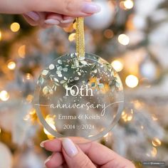 a person holding a glass ornament with flowers on it in front of a christmas tree