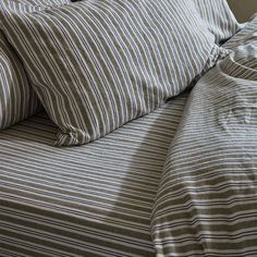 an unmade bed with striped sheets and pillows