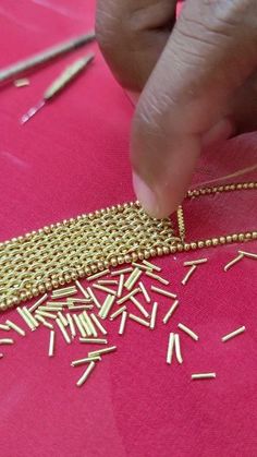 a person is working on a piece of cloth with gold thread and needles in the background