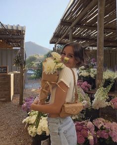 a woman standing in front of flowers holding a paper bag