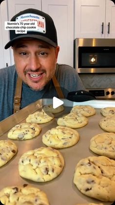 a man with an apron and hat is looking at cookies on a baking sheet in front of him