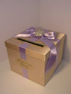 a gold box with purple ribbon and a diamond brooch sits on a white surface