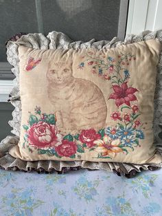 a pillow with a cat on it sitting next to a window sill and flowers