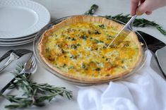 a person cutting into a quiche on top of a table with plates and utensils