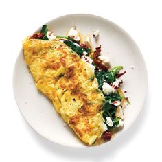 an omelet with spinach and feta cheese on a white plate against a white background