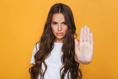 a woman with long brown hair holding her hand up in the air while wearing a white shirt