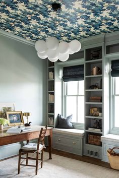 a home office with blue and white wallpaper, built in bookshelves and windows