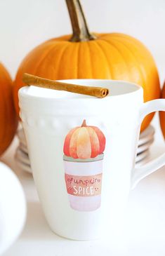 a cup with a cinnamon stick sticking out of it sitting next to some pumpkins