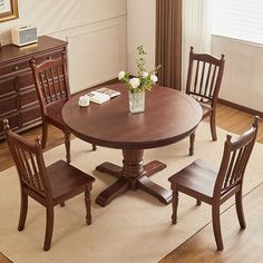 a dining room table with four chairs and a vase on top of it, in front of a window