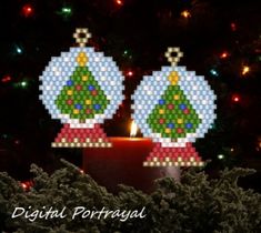 two christmas ornaments sitting on top of a table next to a lit candle in front of a tree