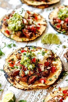 tortillas with meat, salsa and sour cream on a sheet of paper next to lime wedges