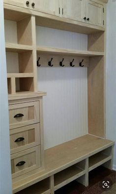 a wooden shelf with drawers and hooks on the wall next to a white cabinet filled with shoes