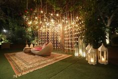 an outdoor area with lights and lanterns on the grass, surrounded by greenery at night