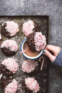 a person is holding a cup of hot chocolate and sprinkles on top of cookies