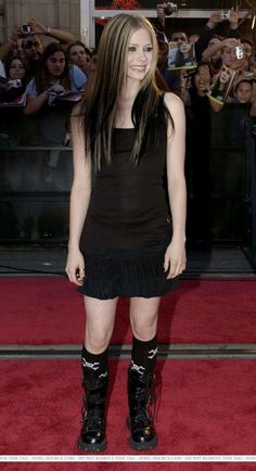 a woman in black dress and boots standing on red carpet