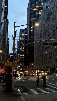 people crossing the street at an intersection in new york city with skyscrapers lit up